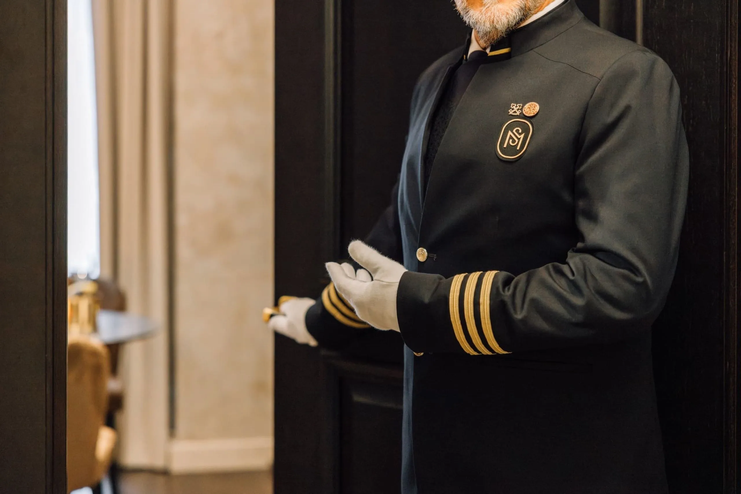 Golden Sleeves Butler in dunkler Uniform mit weißen Handschuhen an einer Suitentür.